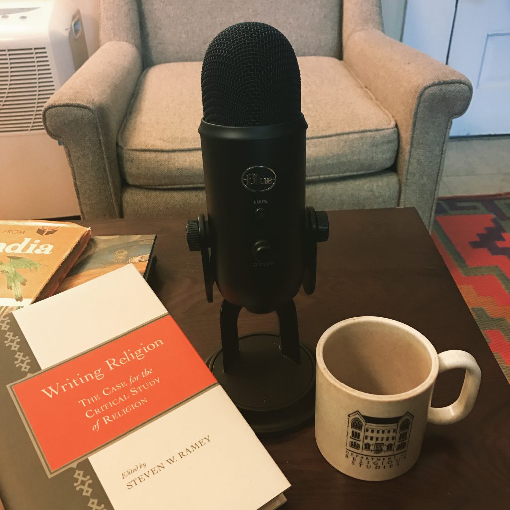 microphone is on a table with a Dept. of Religious Studies at the University of Alabama mug, and the book Writing Religion.